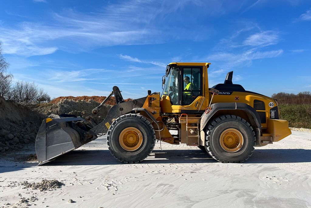 Escavadeira amarela trabalhando em um canteiro de obras ao ar livre sob um céu azul com nuvens.